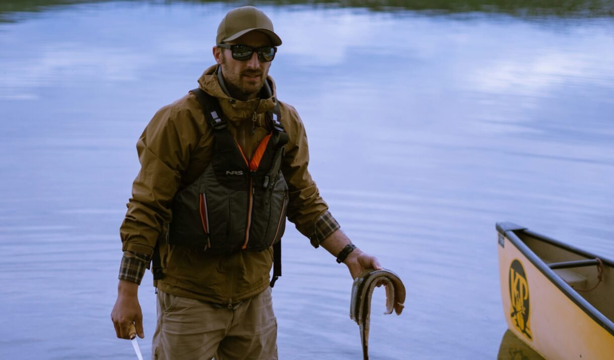 A man holding a fish while standing next to a boat